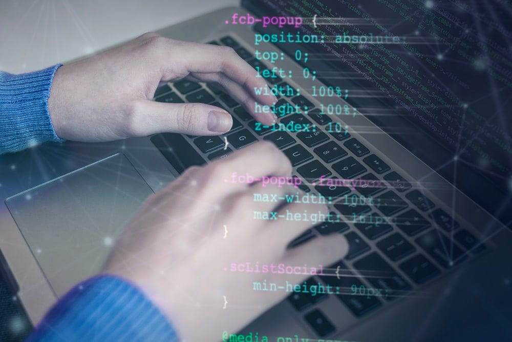 Hands typing on a laptop keyboard with lines of CSS overlaid across the image